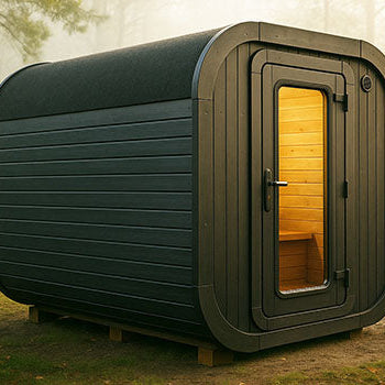Barrel-shaped outdoor sauna with dark wood cladding in misty forest clearing at dawn.