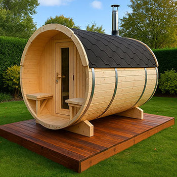 Light wood barrel sauna with black roof on raised wooden deck in a landscaped garden with green hedges.
