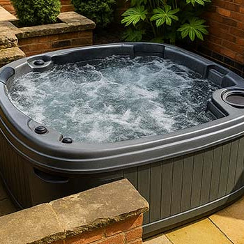 Dark gray hot tub on stone patio corner beside red brick house and garden.