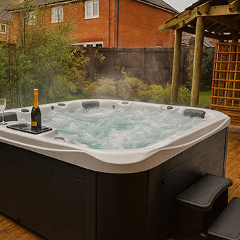Bubbling hot tub on a backyard wooden deck with champagne under a wooden pergola.