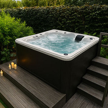 Bubbling white hot tub on dark wooden deck surrounded by garden hedge and lit candles.