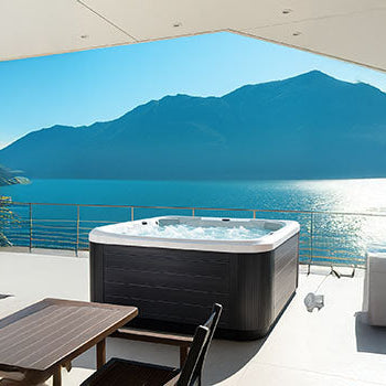 Bubbling hot tub on a terrace with panoramic lake and mountain views under clear blue skies.