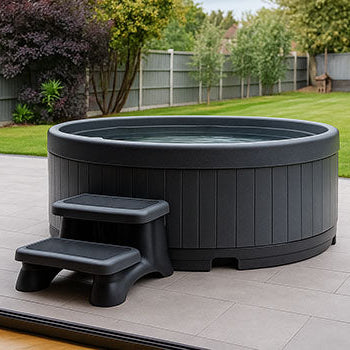 Round rotomoulded hot tub on tiled patio with steps in landscaped backyard.