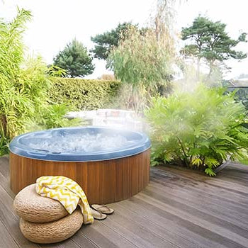 Steaming round hot tub on wooden deck surrounded by tropical garden.