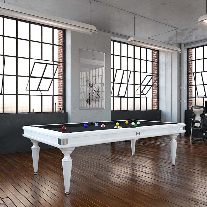 White Etrusco Smile pool table with black cloth, styled in an industrial-inspired interior with tall windows and wooden flooring.