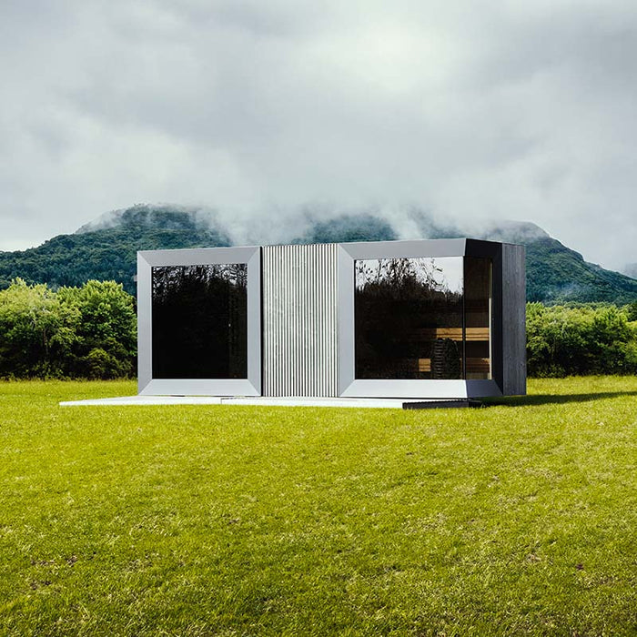 Geneva St. Moritz outdoor sauna with shower room set against dramatic misty mountain backdrop, showcasing sleek mirrored glass panels and contemporary modular design in nature.