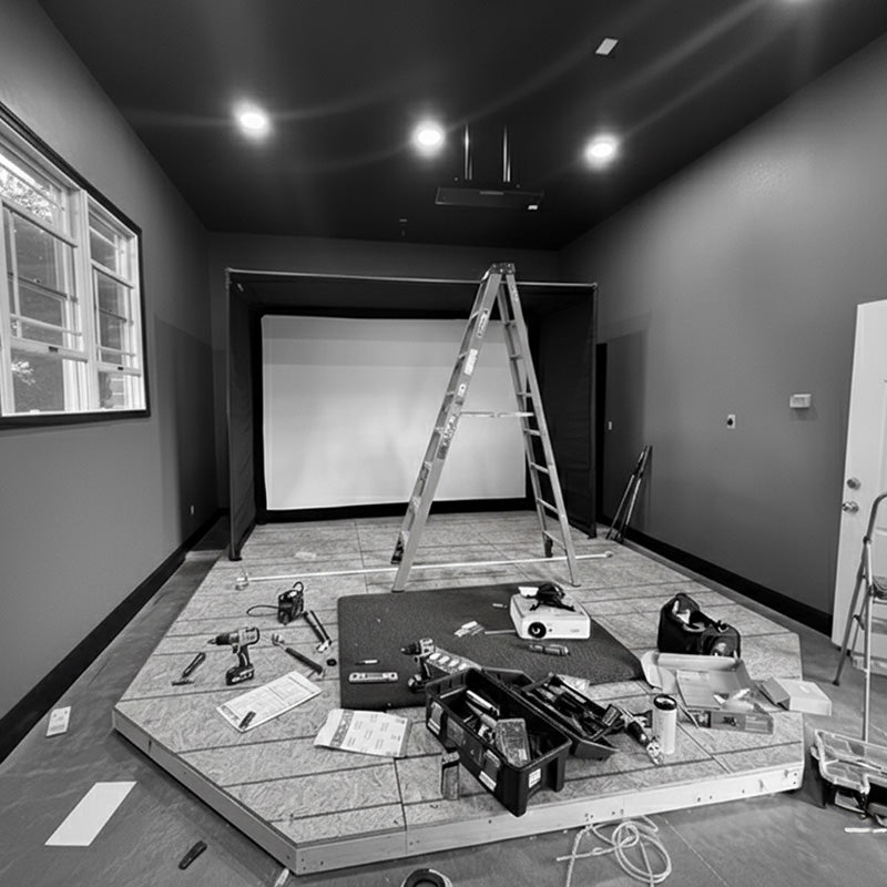 Golf simulator installation in progress inside a home, with tools, projector, and raised platform under construction.