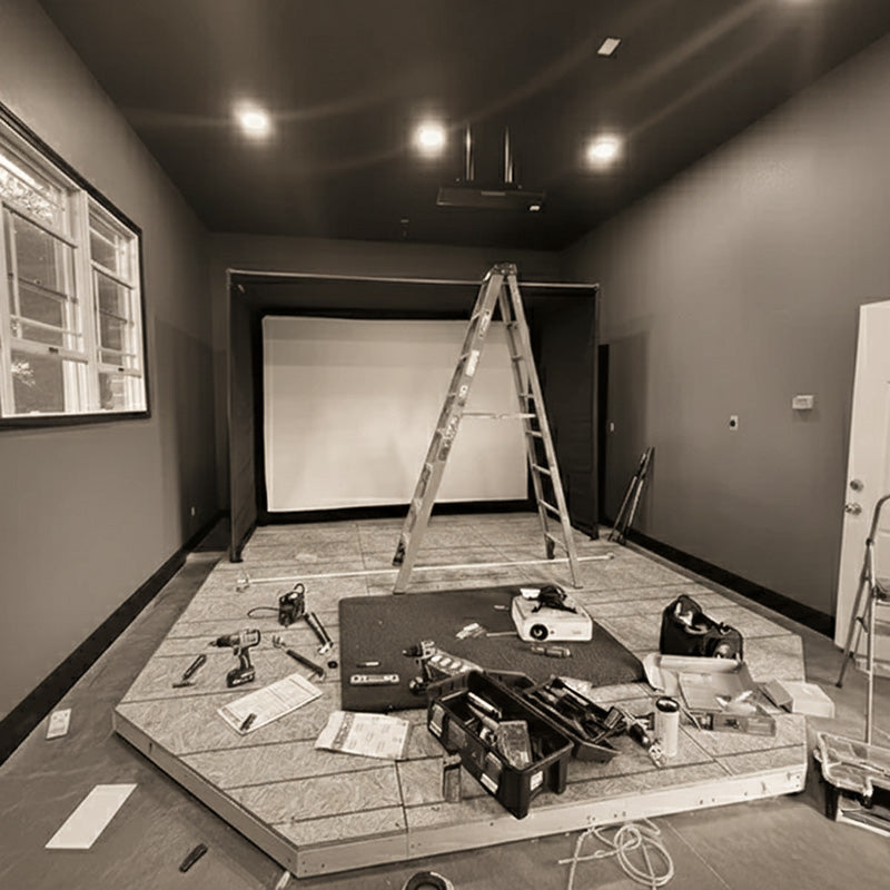 Golf simulator installation in progress inside a home, with tools, projector, and raised platform under construction.