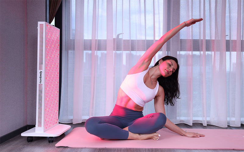 Woman performing side stretch beside Nuvibody CORE 1500 red light therapy panel, showcasing full-body light exposure in a serene wellness setting.