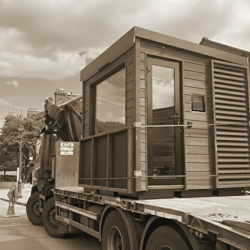 Modern outdoor sauna unit securely transported on a flatbed truck for delivery and installation.