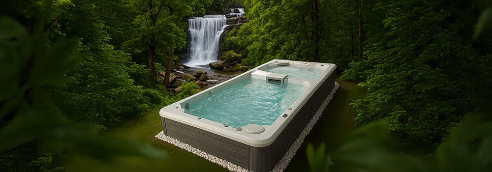 Acrylic swim spa in tropical forest setting with waterfall in background.