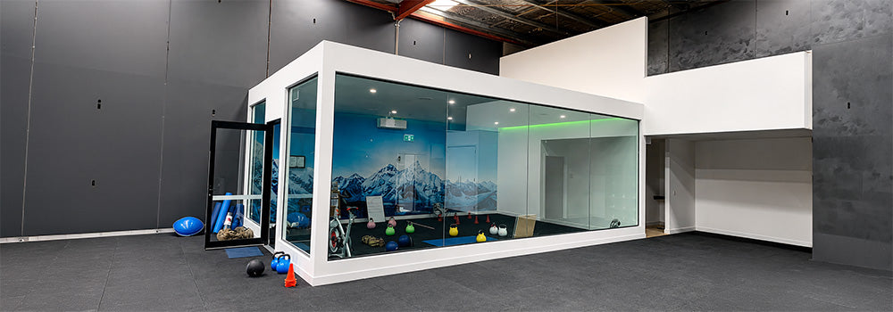 The Altitude Centre white modular training pod with glass walls and mountain mural interior, kettlebells and gym equipment in the foreground.