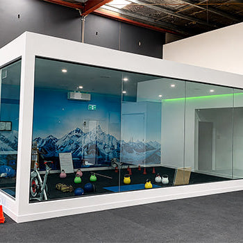 The Altitude Centre white modular training pod with glass walls and mountain mural interior, kettlebells and gym equipment in the foreground.