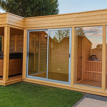 Modern backyard sauna and hot tub cabin with glass doors, natural wood finish, and green lawn.