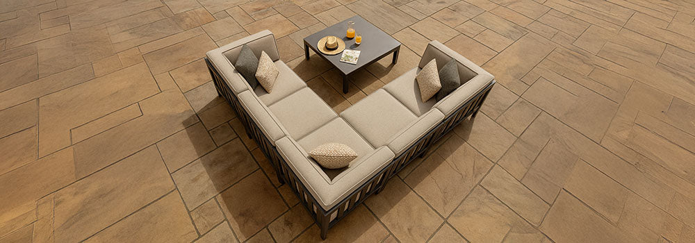 Beige L-shaped garden sofa set with a low coffee table on a warm stone patio under natural daylight.