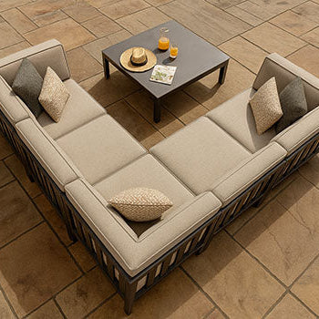 Beige L-shaped garden sofa set with a low coffee table on a warm stone patio under natural daylight.