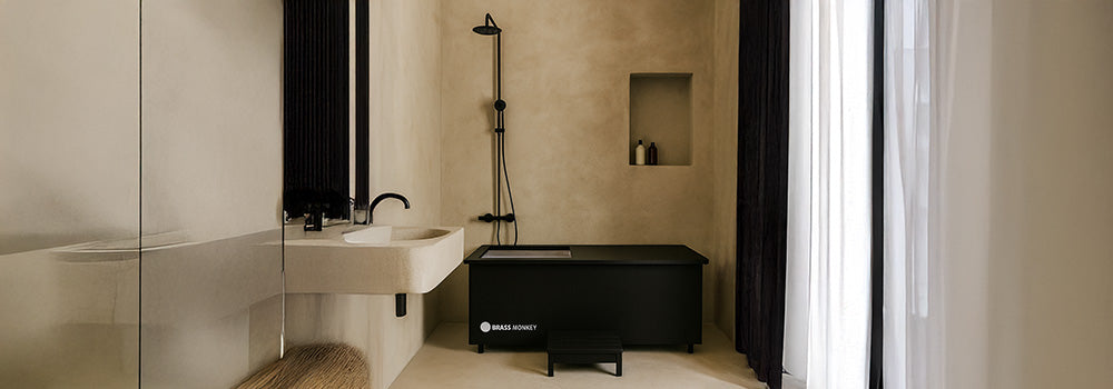Matte black Brass Monkey ice bath with steps in a minimalist beige bathroom with walk-in shower and floating sink.