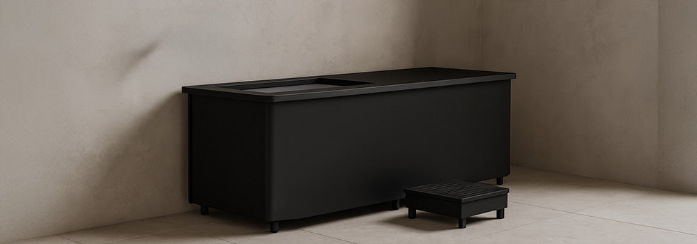 Black ice bath in a minimalist beige bathroom with matte fixtures and folded towels.
