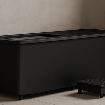 Black ice bath in a minimalist beige bathroom with matte fixtures and folded towels.