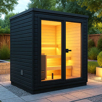 Modern black outdoor sauna on a landscaped backyard patio at dusk with warm interior lighting and lush greenery