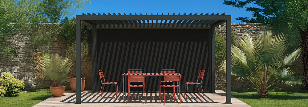 Black pergola casting striped shadows over terracotta dining set on wooden deck with stone wall and tropical plants.