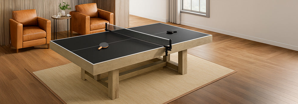 Black table tennis table with light wood frame in cozy living room featuring caramel leather chairs, wood paneling, and large window with curtains.