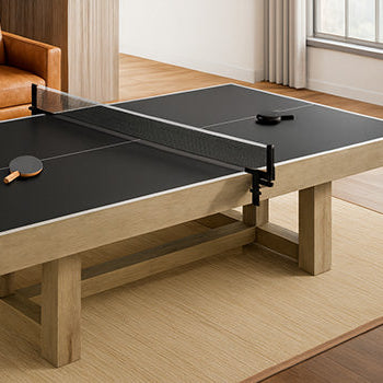 Black table tennis table with light wood frame in cozy living room featuring caramel leather chairs, wood paneling, and large window with curtains.