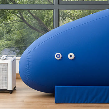 Soft hyperbaric oxygen chamber in a bright therapy room with large windows, wood floors, and garden views.