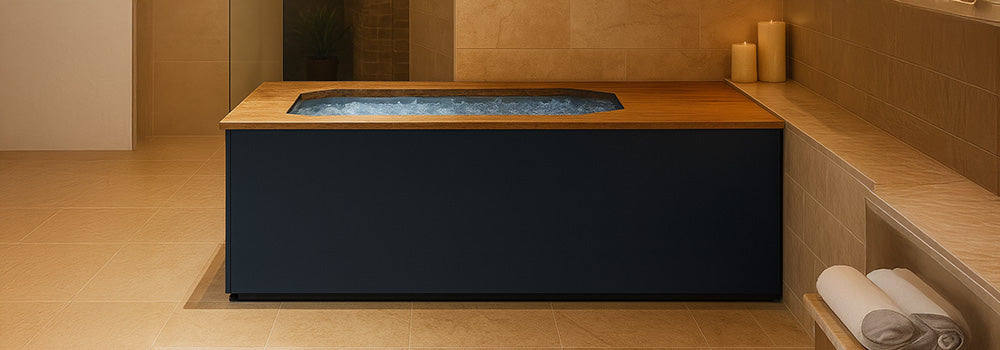Brass Monkey ice bath with wooden ledge filled with ice in a tranquil spa room with beige stone walls, candles, and warm lighting.
