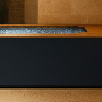 Brass Monkey ice bath with wooden ledge filled with ice in a tranquil spa room with beige stone walls, candles, and warm lighting.