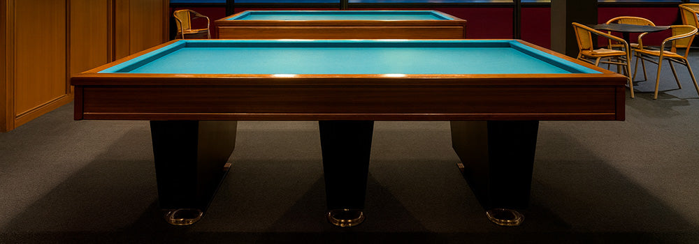 modern carom pool tables with blue felt in a billiards lounge overlooking a city skyline and bridge through large windows at night.