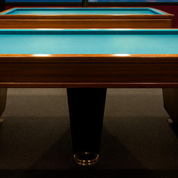 modern carom pool tables with blue felt in a billiards lounge overlooking a city skyline and bridge through large windows at night.