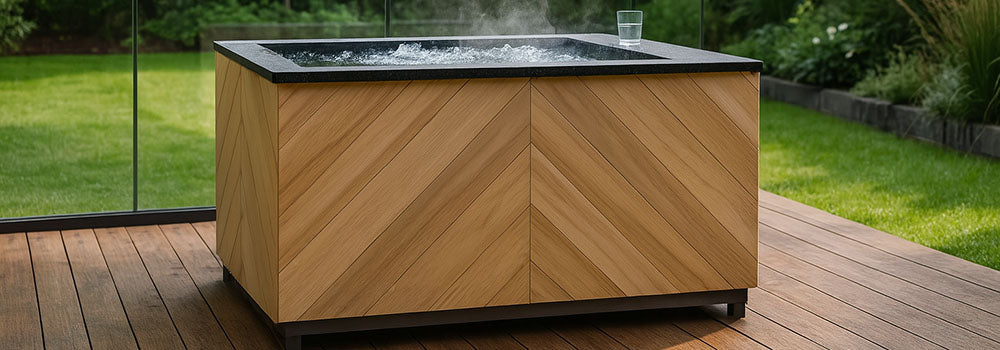Modern chevron-panelled ice bath on a sleek wooden deck with lush green garden and glass railing backdrop.