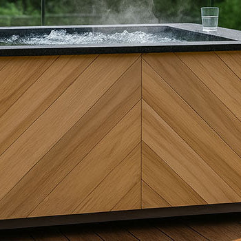 Modern chevron-panelled ice bath on a sleek wooden deck with lush green garden and glass railing backdrop.
