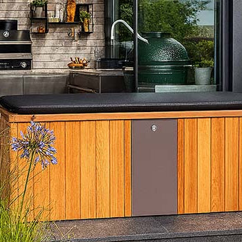 Cedar-clad ice bath with black cover in a modern garden kitchen patio surrounded by lush plants and water feature.