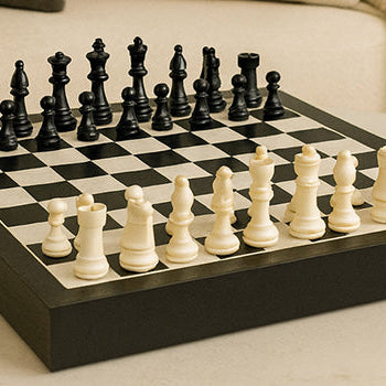 Classic black and white chess set on a marble coffee table in a neutral-toned living room with plush seating and a vintage mirror.