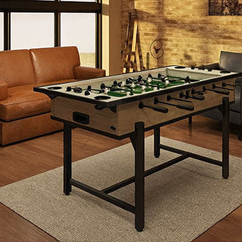 Classic foosball table in a warm industrial loft with exposed brick walls, leather sofa, and large windows.