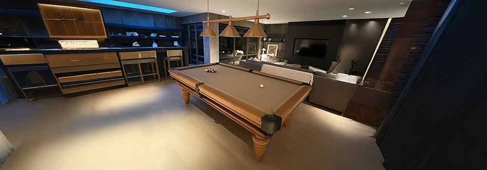 rustic wood pool table with gray felt in a bright farmhouse-style game room with large windows and industrial lighting.