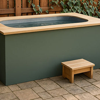 Minimalist cold plunge tub with wood top on a stone patio, surrounded by ivy-covered fencing and garden accents.