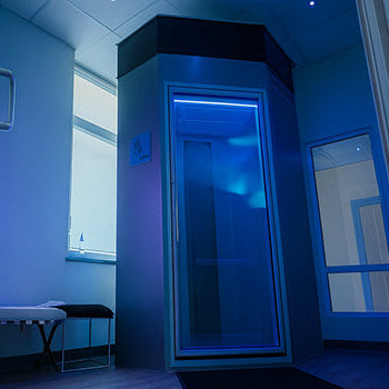 Futuristic cryo chamber in a cool-toned wellness room with blue LED lighting and modern glass walls.
