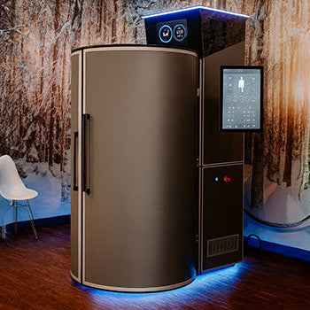 Modern cryotherapy chamber in a warm-toned room with winter forest mural and wood flooring.