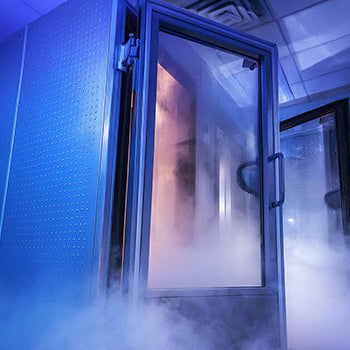 Futuristic cryotherapy chamber with mist and glowing blue-pink lighting in a high-tech room.
