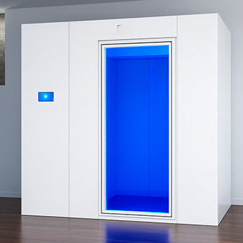 Modern white cryotherapy chamber with blue-lit interior in a minimalist room with dark wood floors and stone accent wall.