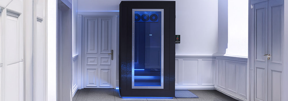 Black cryotherapy chamber with blue-lit interior in a refined wellness room with white paneled walls and modern finishes.