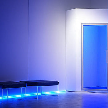 Futuristic cryotherapy chamber in a dark tiled room with blue LED ambient lighting and minimalist decor.
