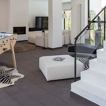 Designer foosball table in a bright, modern open-plan living room with white walls, glass railings, and zebra print rug.