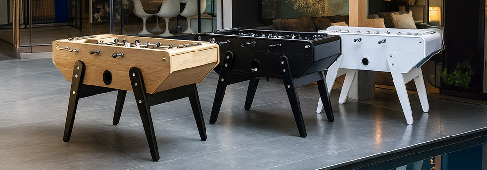 trio of designer foosball tables in natural, black, and white finishes beside a modern indoor pool.