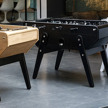 trio of designer foosball tables in natural, black, and white finishes beside a modern indoor pool.