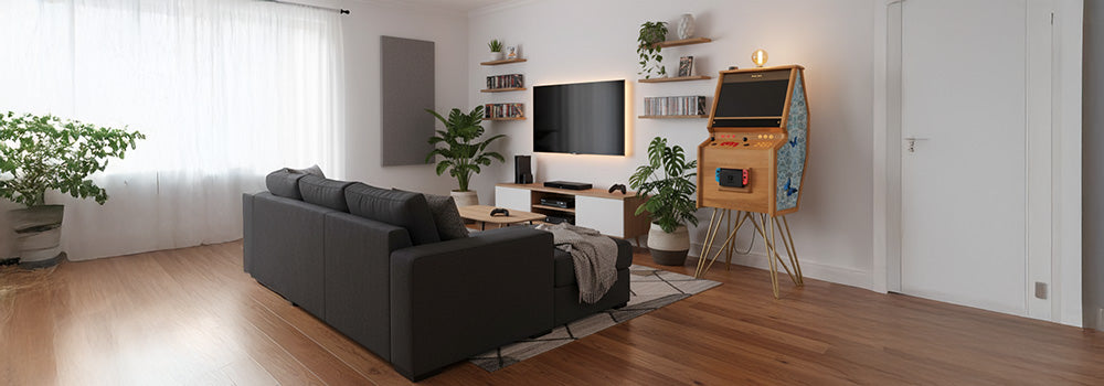 Retro-inspired wooden arcade machine with vibrant side panel artwork, classic joystick controls, and integrated Nintendo Switch console, styled in a modern living room setup with plants and wood flooring.