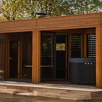 Modern flat-roof garden room with hot tub and wooden deck surrounded by autumn trees.